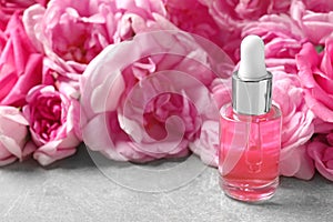 Bottle of rose essential oil and fresh flowers on table