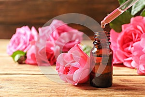 Bottle of rose essential oil, pipette and flowers on wooden table