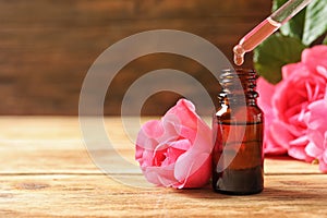 Bottle of rose essential oil, pipette and flowers on wooden table