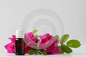 A bottle of rose essential oil with small rose blossoms on a white background