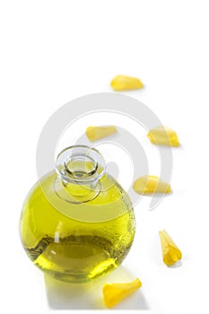 A bottle of rose essential oil with yellow rose petals on a white background