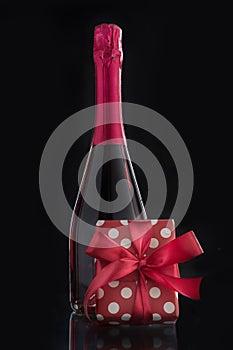 Bottle of rose sparkling wine with romantic gift and red bow. Vertical format. Isolated on black. Romantic present