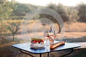 Bottle of rose wine and two full glasses of wine on table in heart of Provence, France with french bread, cheese, ham, grapes and