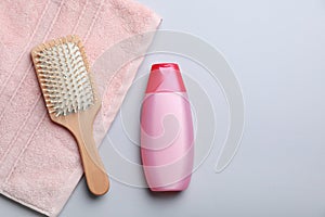 Bottle with shampoo, towel and brush on color background, flat lay.