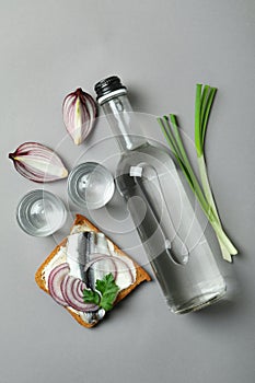 Bottle and shots of vodka, and snacks on gray background