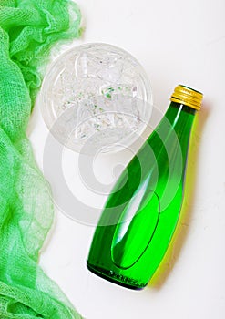 Bottle of sparkling mineral water with glass of ice and green cloth on white