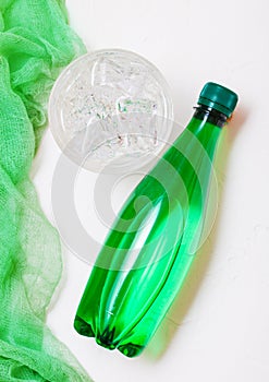 Bottle of sparkling mineral water with glass of ice and green cloth on white