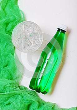 Bottle of sparkling mineral water with glass of ice and green cloth on white