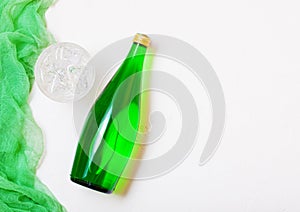 Bottle of sparkling mineral water with glass of ice and green cloth on white