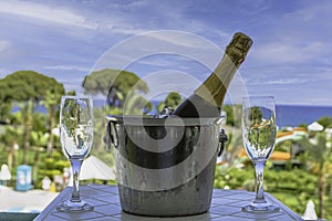 A bottle of sparkling wine in an ice bucket and two glasses on the balcony against the background of the sea and the