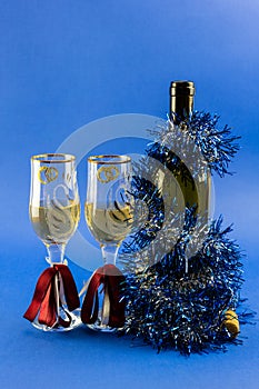 A bottle of sparkling wine with two glasses decorated with New Year`s tinsel