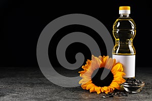 Bottle of sunflower cooking oil, seeds and beautiful flower on grey table against black background. Space for text