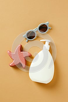 Bottle with sunscreen body lotion, sand toy and baby sunglasses on sand color background. Baby suntan cosmetics design