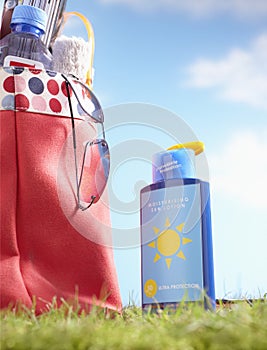 Bottle of suntan lotion and bag with beach items in grass close-up