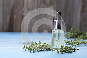 Bottle of thyme essential oil and fresh plant on light blue wooden table, space for text