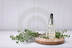 Bottle of thyme essential oil and fresh plant on white wooden table, space for text