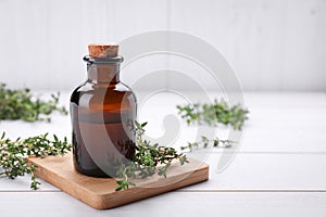 Bottle of thyme essential oil and fresh plant on white wooden table, space for text