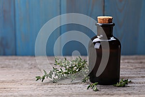 Bottle of thyme essential oil and fresh plant on wooden table, space for text