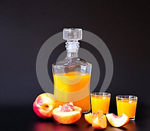 A bottle and two glasses of peach liqueur and sliced ripe fruits on a black background