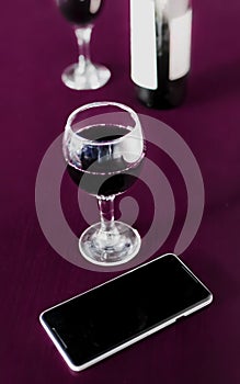 Bottle and two glasses of red wine and a mobile phone on marsala color wodden table and blurred background. Alcohol drink and smar