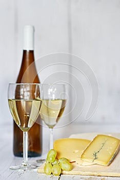 Bottle and two glasses of white wine, white grape and blue cheese on a wooden background