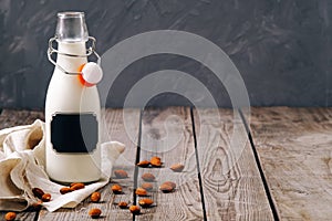 Bottle of vegan plant milk and almond nuts on wooden table on grey background. Banner with copy space. Dairy free milk substitute