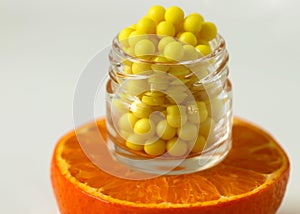 A bottle of vitamin C pills stands on a fresh slice of orange close-up on a white background. The concept of the natural