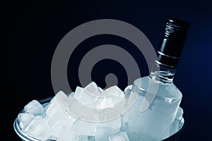 Bottle of vodka in metal bucket with ice on black background, closeup. Space for text
