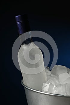 Bottle of vodka in metal bucket with ice on dark background