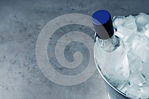 Bottle of vodka in metal bucket with ice on grey table, above view. Space for text