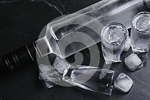 Bottle of vodka and shot glasses with ice on black table, above view