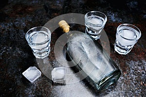 Bottle of vodka with shot glasses and ice. On stone background.