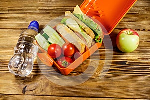 Bottle of water, apple and lunch box with sandwiches and fresh vegetables on wooden table