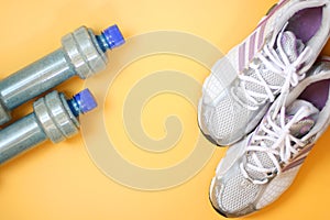 Bottle for water, dumbbells and sports shoes on a yellow background.Top view with copy space.
