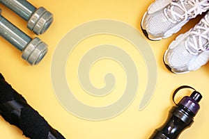 Bottle for water, dumbbells and sports shoes on a yellow background.Top view with copy space.