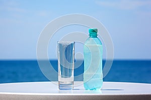 Bottle of water and glass on table under open sky