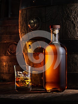 Bottle of whisky and glass of whisky. Old wooden cask at the background