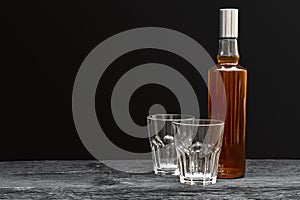 Bottle of whisky with two empty glasses on black background. Space for text
