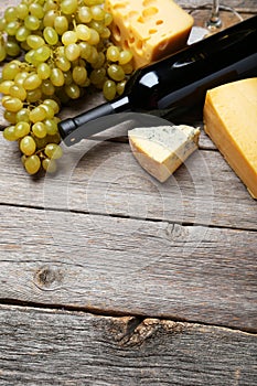 Bottle of white wine, cheeses and grapes on the grey wooden background