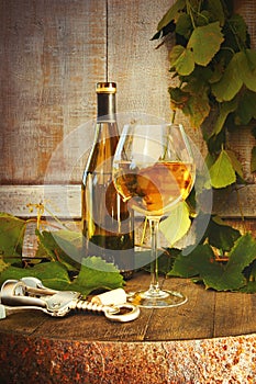 Bottle of white wine with glass on barrel