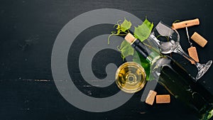 A bottle of white wine with glasses and grapes. Leaves of grapes. Top view. On a black wooden background.