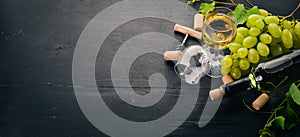 A bottle of white wine with glasses and grapes. Leaves of grapes. Top view. On a black wooden background.