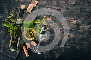 A bottle of white wine with glasses and grapes. Leaves of grapes. Top view. On a black wooden background.