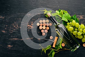 A bottle of white wine with glasses and grapes. Leaves of grapes. Top view. On a black wooden background.
