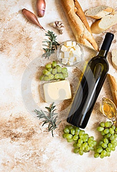 A bottle of white wine, grapes, cheese, butter, honey, baguette, shallot and rosemary