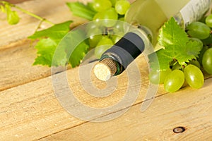 Bottle of white wine, grapes and leaves on wooden table