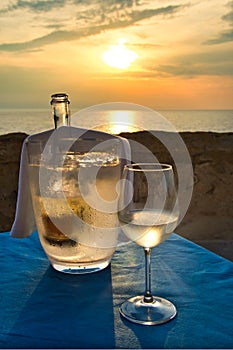 Bottle of white wine, in the ice bucket with a glass alongside, at sunset by the sea in Italy.