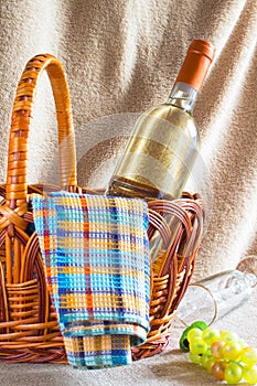 Bottle of white wine, napkin and bunch of grapes in a wicker basket