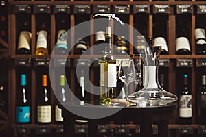 Bottle of white wine on the table next to decanter and glasses over shelf background.