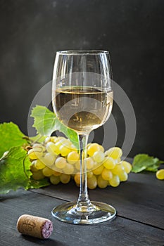Bottle of white wine with wineglass, ripe grape on black wooden table